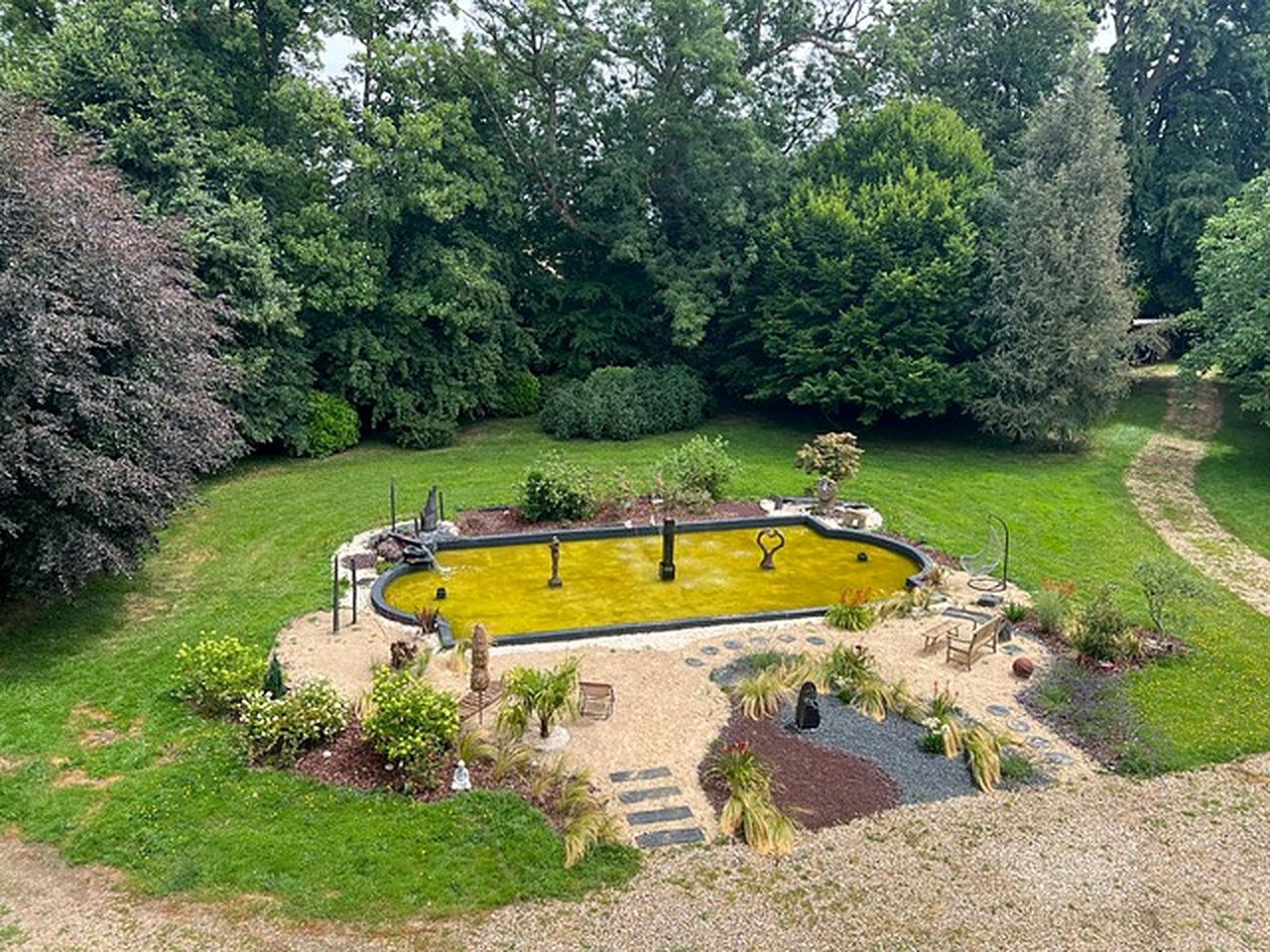 Bassin naturel paysagé entouré de graminées et de sculptures dans le parc
