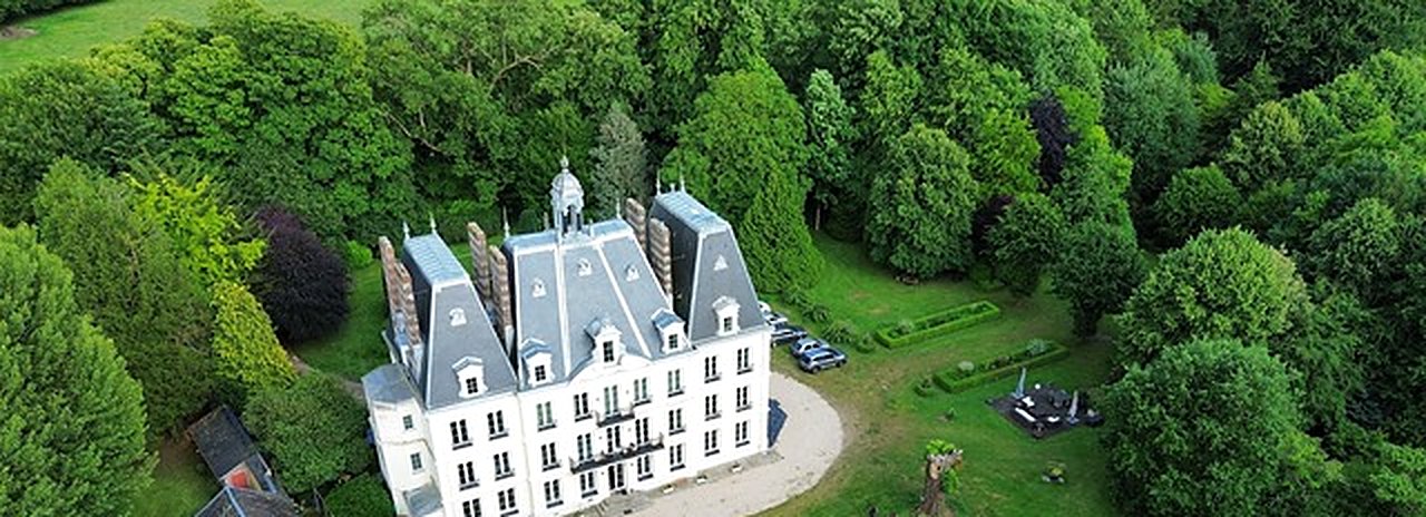 Vue aérienne du château RenéeSens, toits d'ardoise et façade claire au cœur d'un parc boisé en Normandie