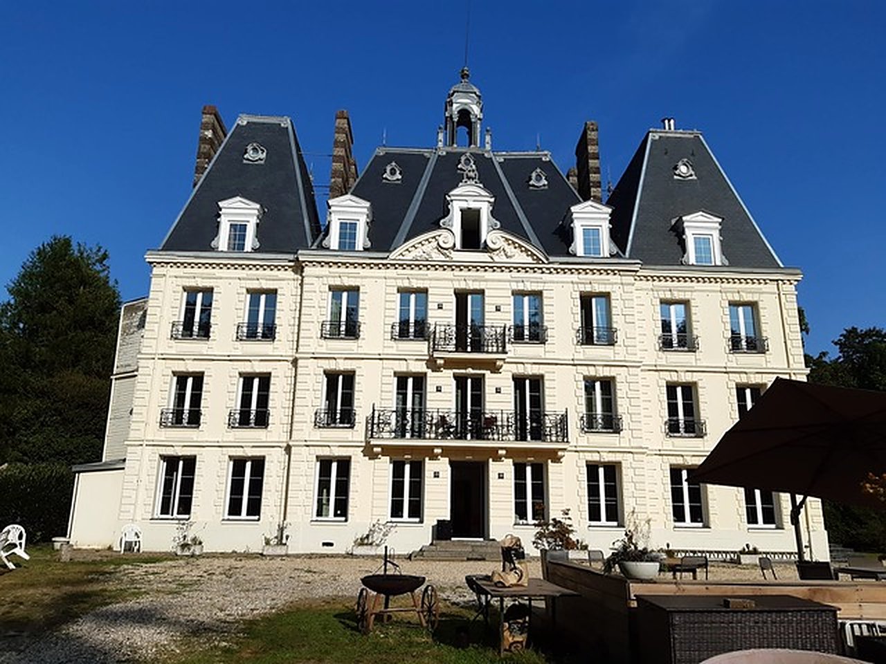 Façade du château de Bimare : pierre claire, balcons en fer forgé et toits d'ardoise à la Mansart sous un ciel bleu